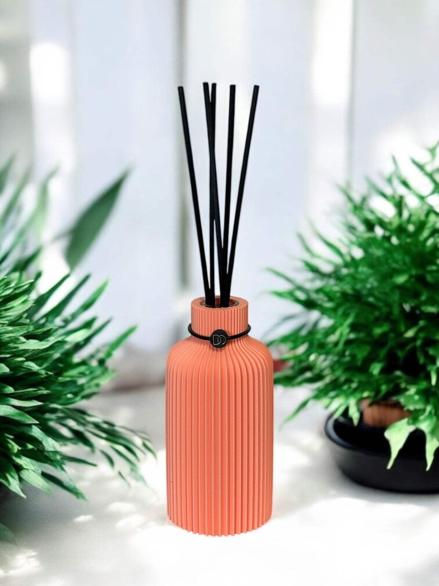 Diffuseur minimalist au design élégant avec bâtons noirs, entouré de verdure.