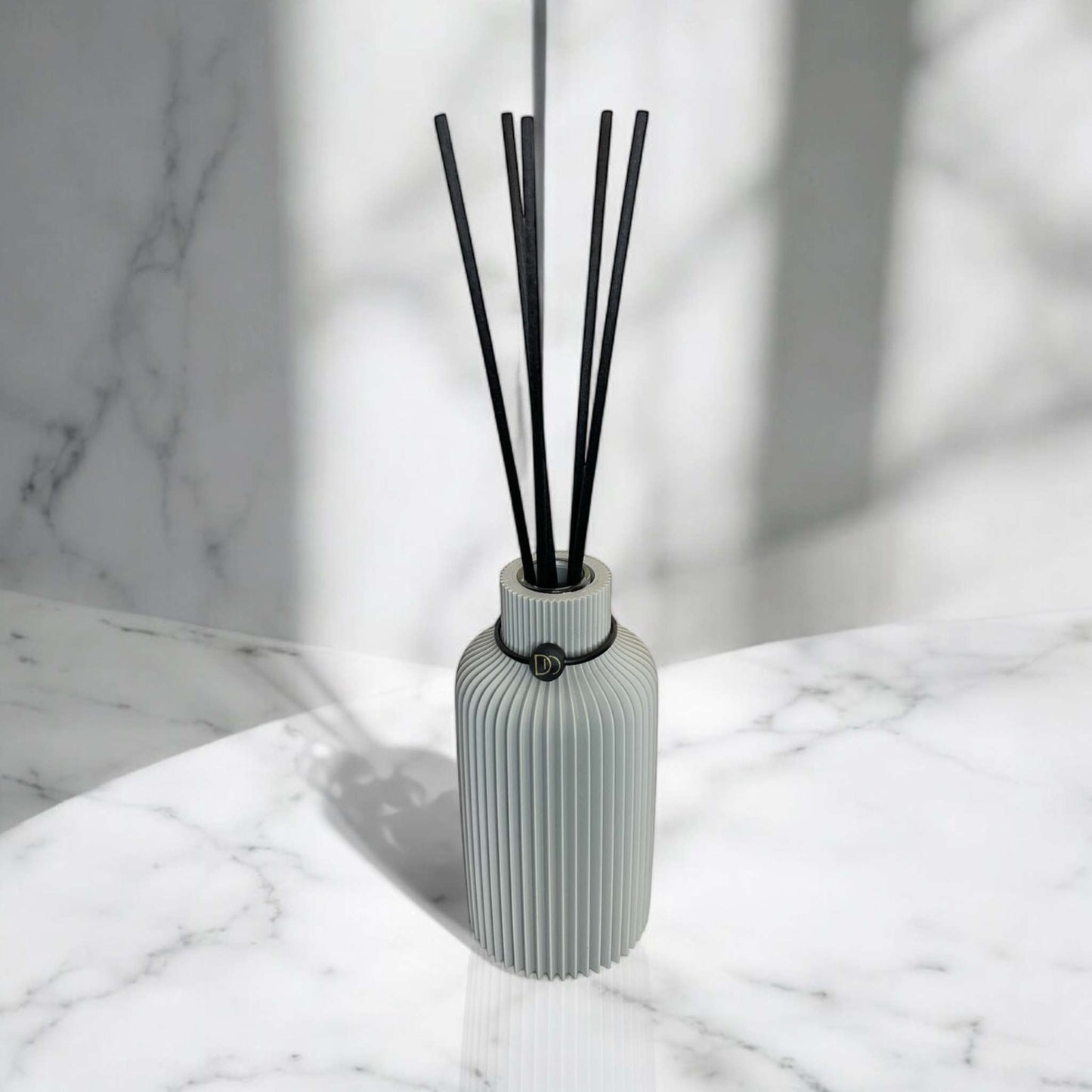Elegant minimalist diffuser with black reeds on marble surface.