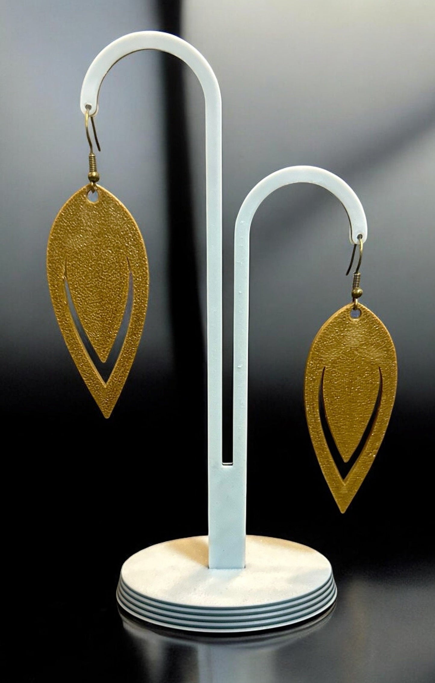 Boucles d'oreilles Luma en bronze texturé, design goutte ajourée, sur présentoir blanc.