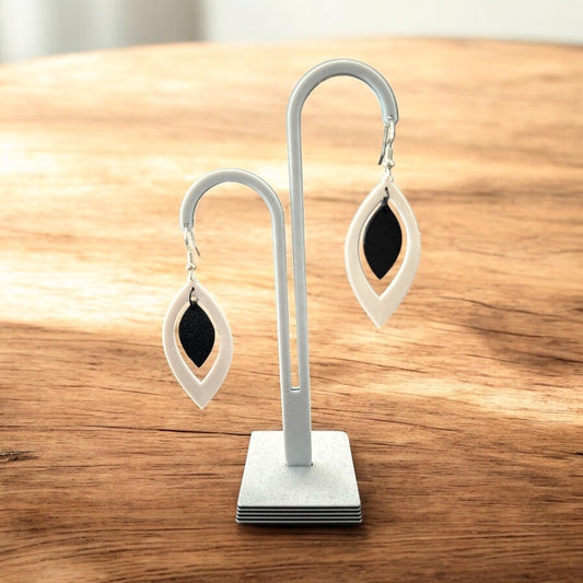 Boucles d'oreilles Élégance Bicolore en forme de goutte allongée, blanc nacré et noir profond, sur porte-bijoux.