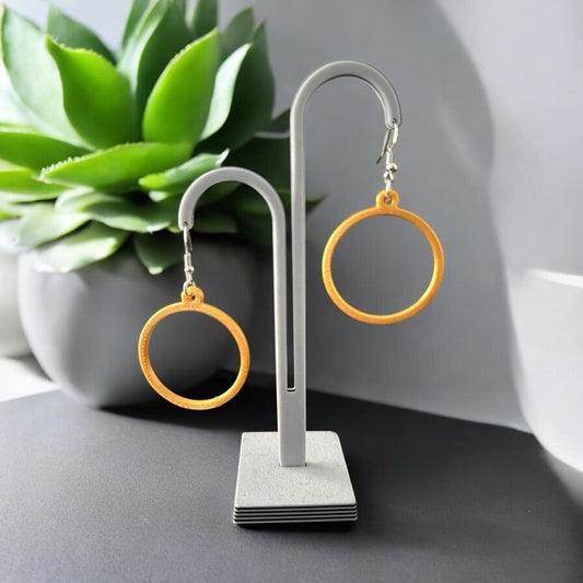 Boucles d'oreilles créoles dorées légères et brillantes sur présentoir, design moderne, éco-responsables en PLA avec attache en argent ou plaqué or.