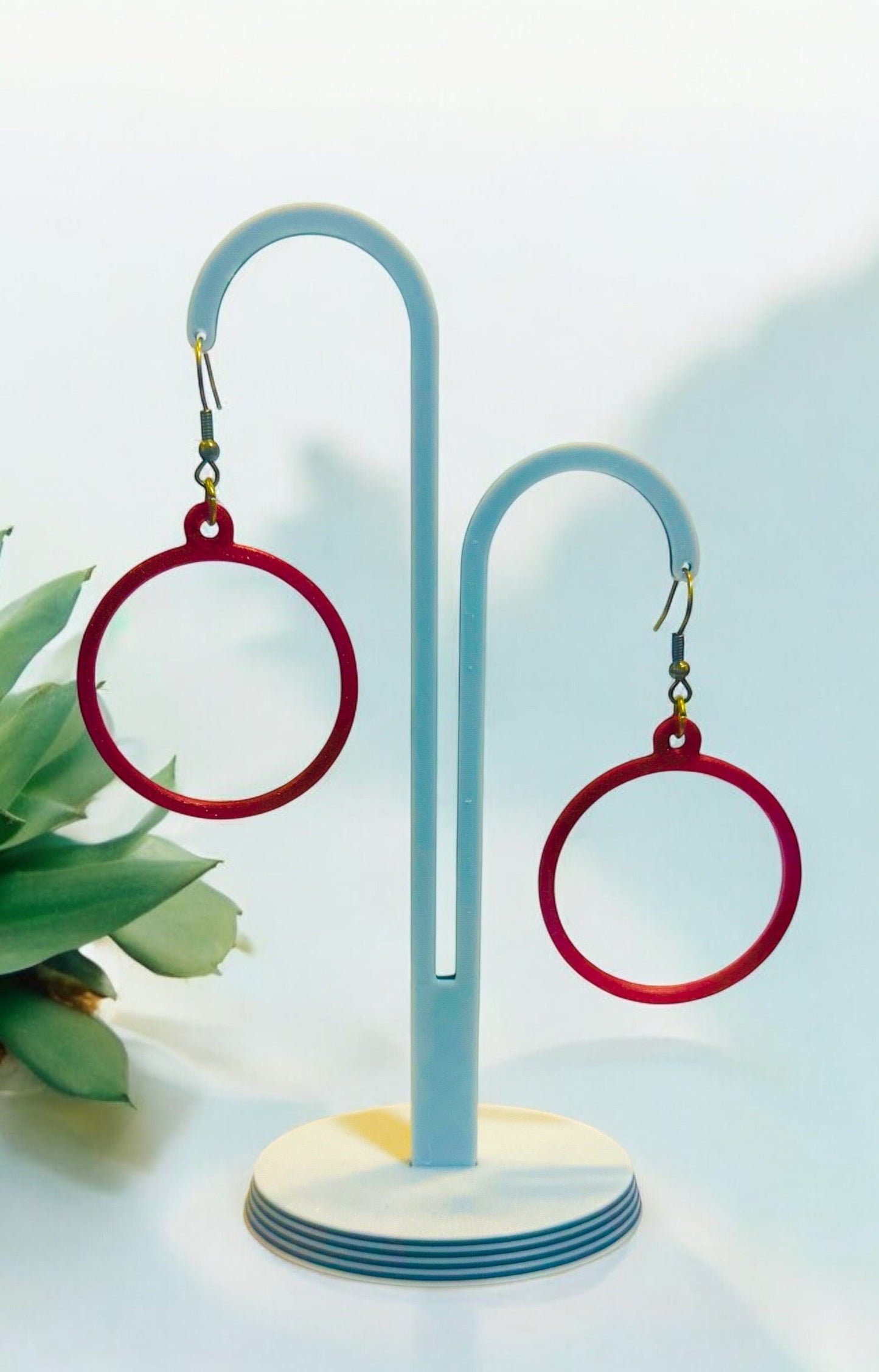 Boucles d'oreilles créoles rouges sur support, design circulaire moderne, légères et brillantes.