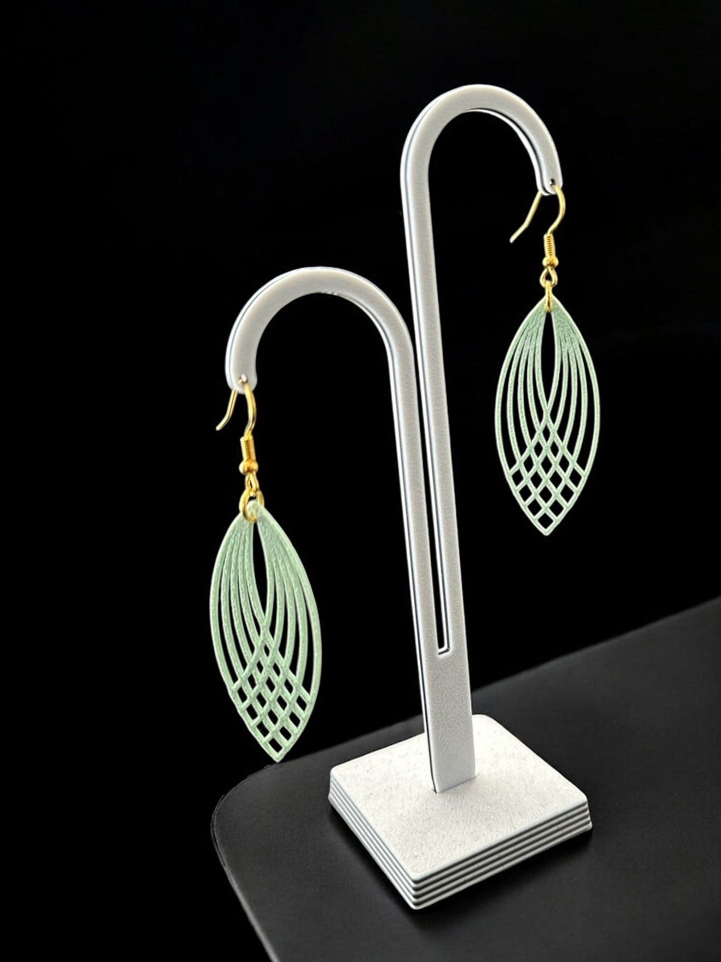 Boucles d'oreilles Pluma légères, design plume géométrique ajourée, couleur menthe givrée, sur présentoir noir.