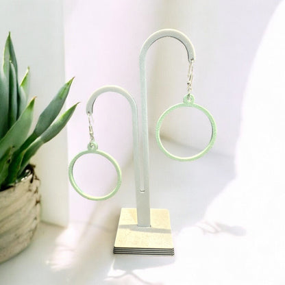 Boucles d'oreilles Créoles en PLA biosourcé, légères et scintillantes, sur présentoir, avec attache en argent.