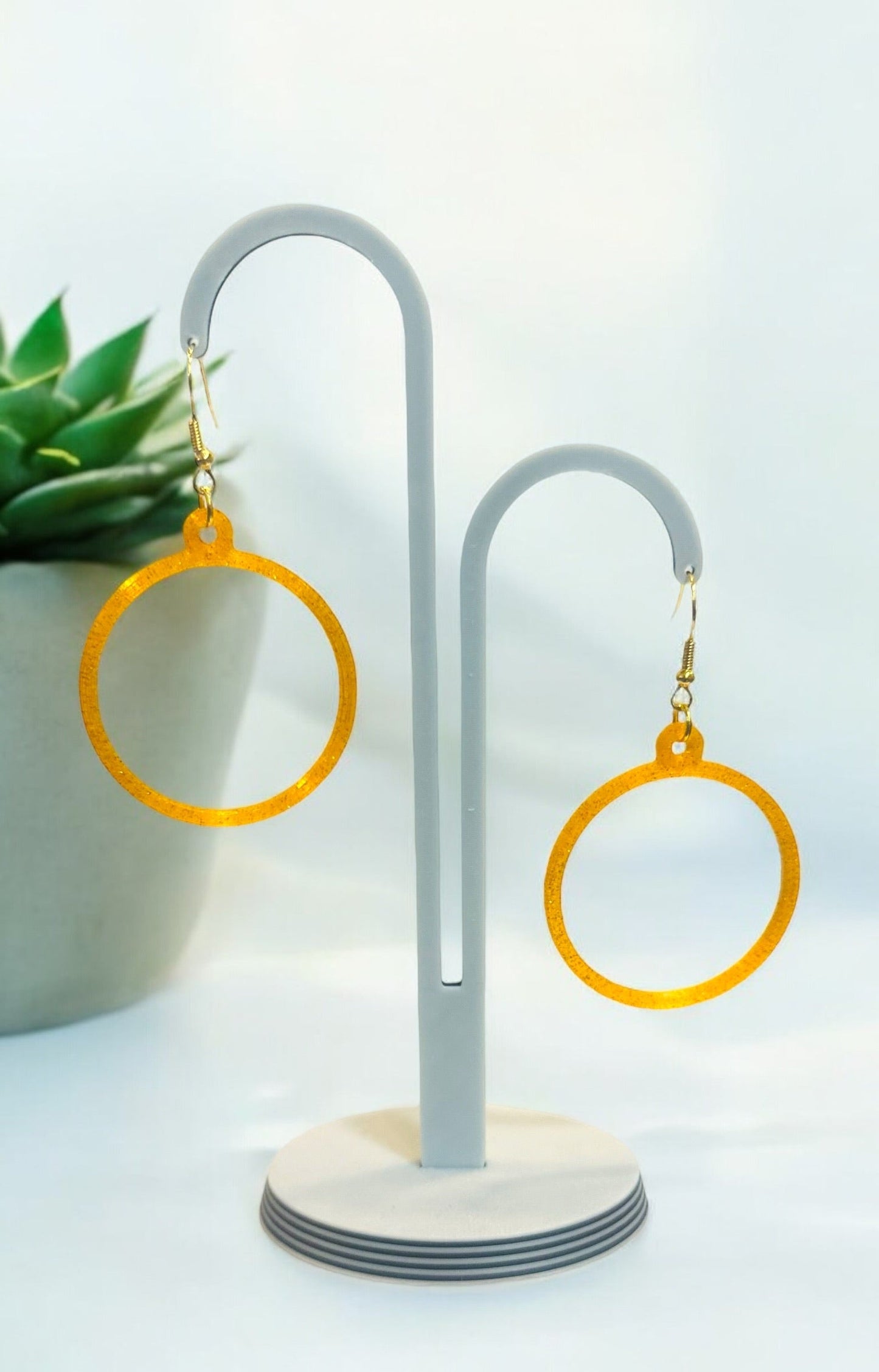 Boucles d'oreilles créoles dorées brillantes sur présentoir, design circulaire léger et moderne.