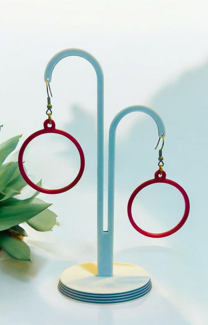 Boucles d'oreilles créoles rouges sur support, design circulaire moderne, légères et brillantes.